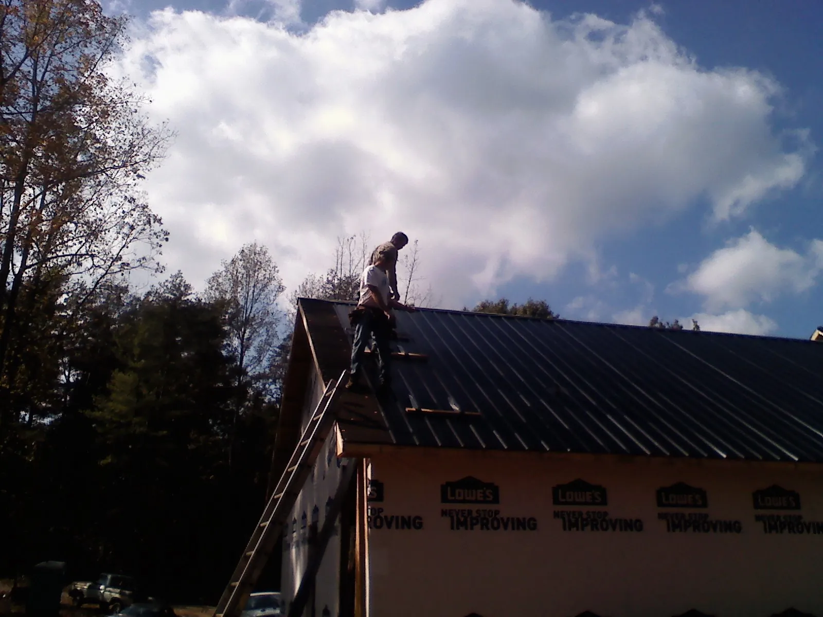 Roofer fastening dark metal panels high against a cloudy sky, from a Roof Inspection job in New Haven